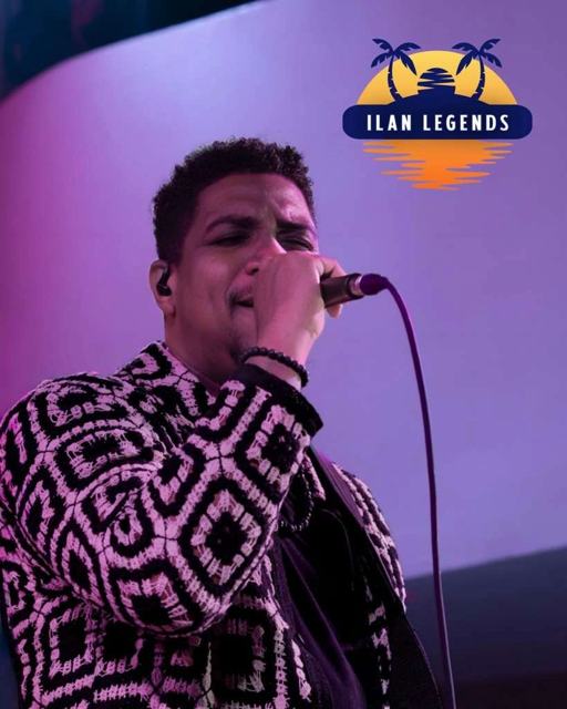 A vocalist in a patterned shirt performing under purple light